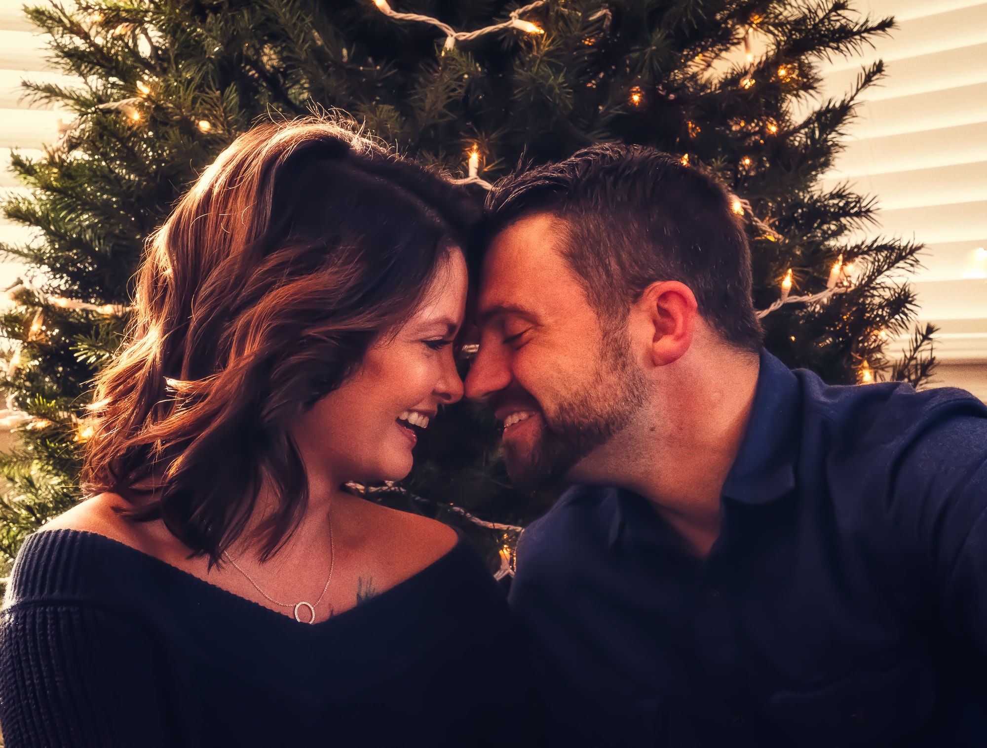 Couple smiling together by a lit Christmas tree